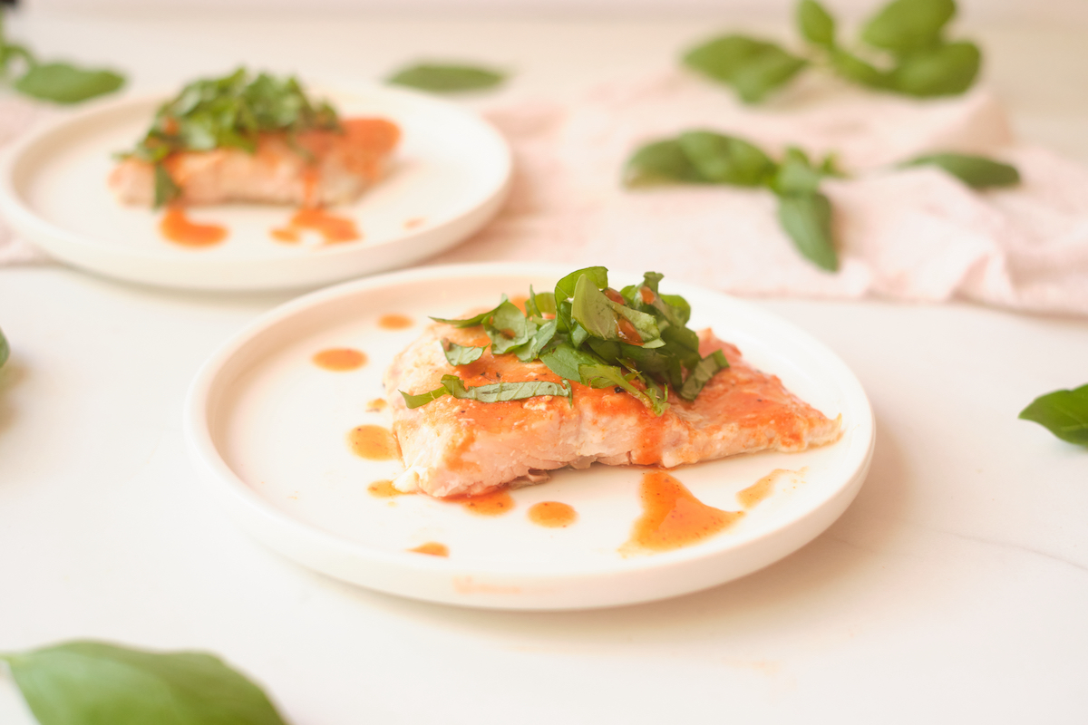 Side view of honey sriracha salmon fillets with basil, plated with basil leaves strewn about