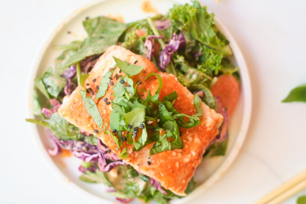 A fillet of salmon piled with fresh basil sits atop an asian sesame salad with fresh veggies