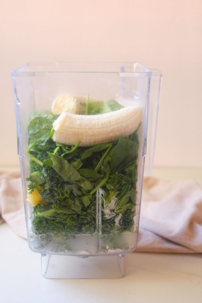 Ingredients for a post workout green smoothie in a blender including banana, pineapple and greens