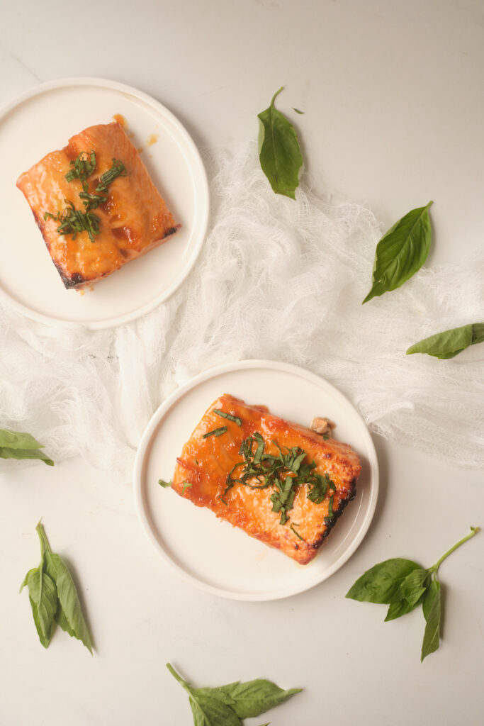 Birds eye view of apricot glazed salmon with basil plated and sitting on a table with basil leaves strewn about