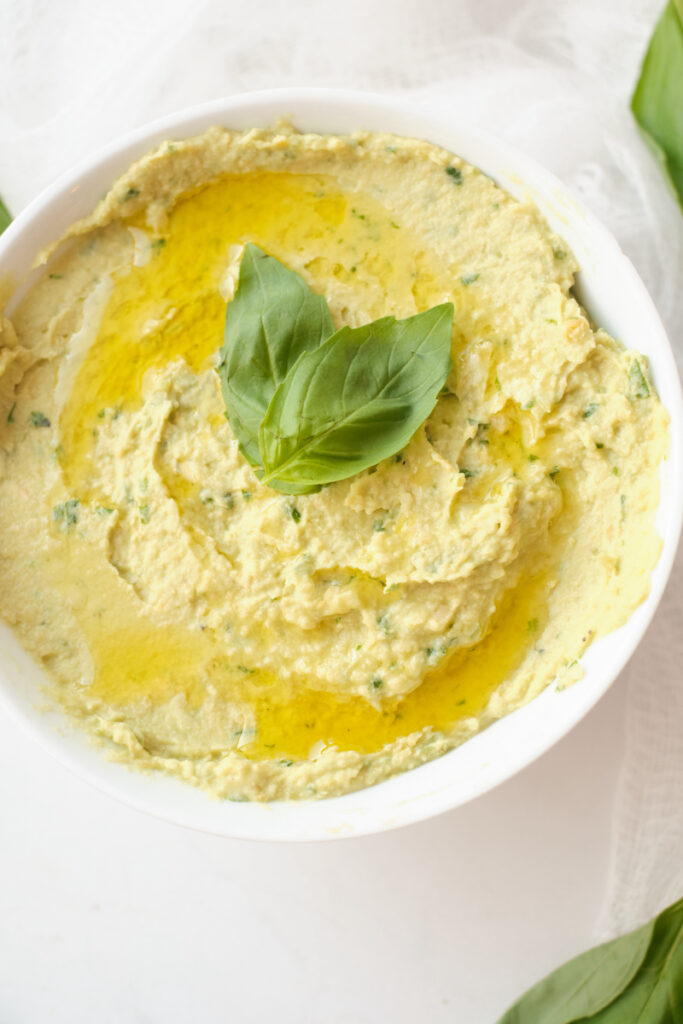 Close up of basil avocado hummus in a serving dish topped with a fresh basil leaf