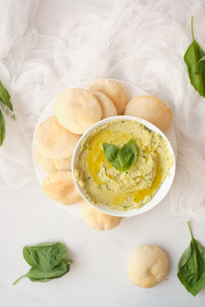 Avocado hummus with basil in a serving bowl surrounded by mini pita rounds