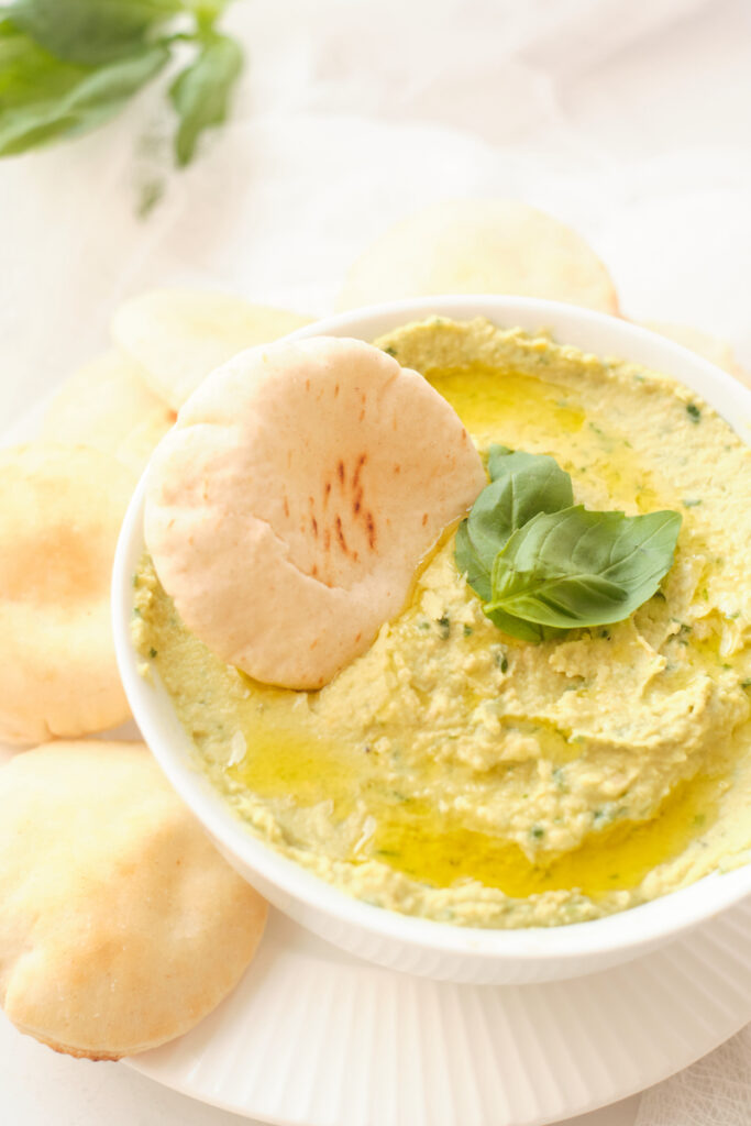 A pita round in a bowl of freshly made avocado hummus with basil dip