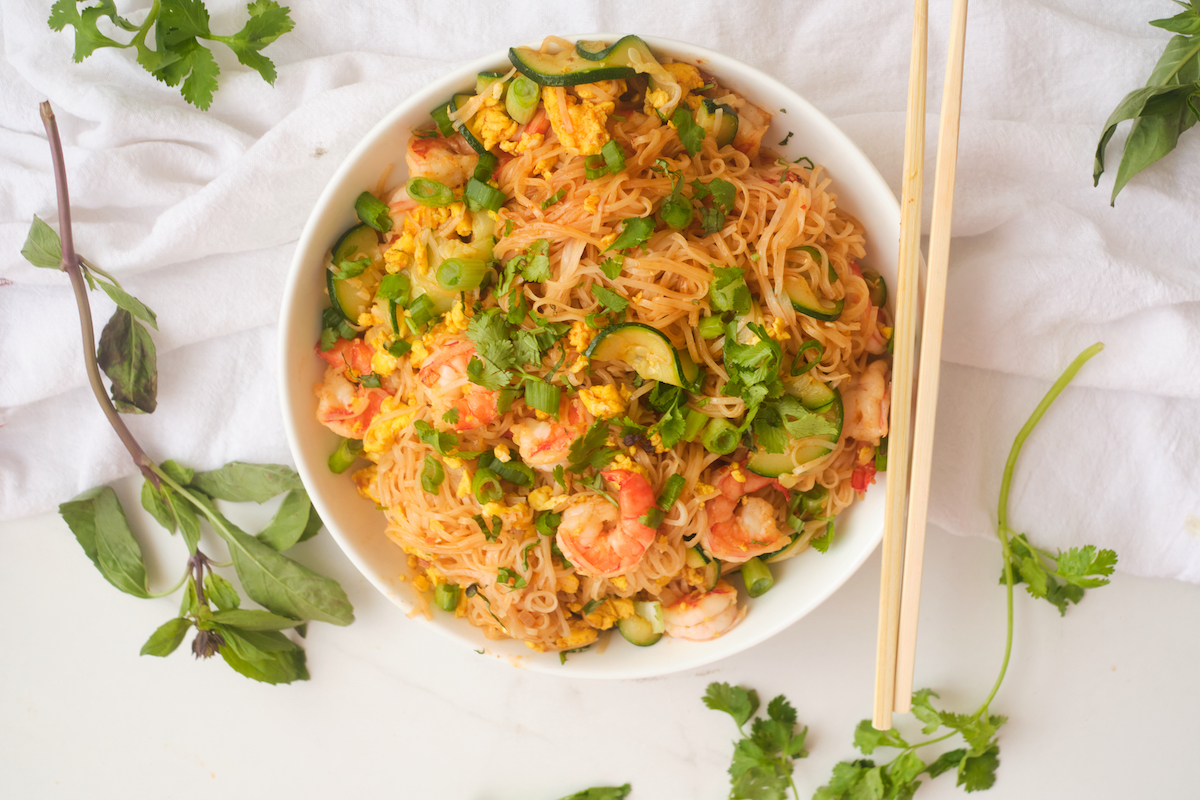 Spicy shrimp noodles in a bowl with chopsticks and fresh herbs