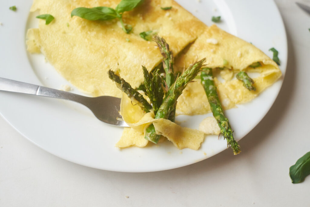A fork digs into an asparagus omelette with goat cheese and basil on a plate