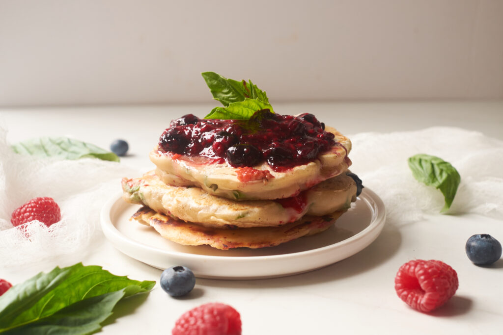 Stack of lemon basil pancakes topped with butter and basil berry compote