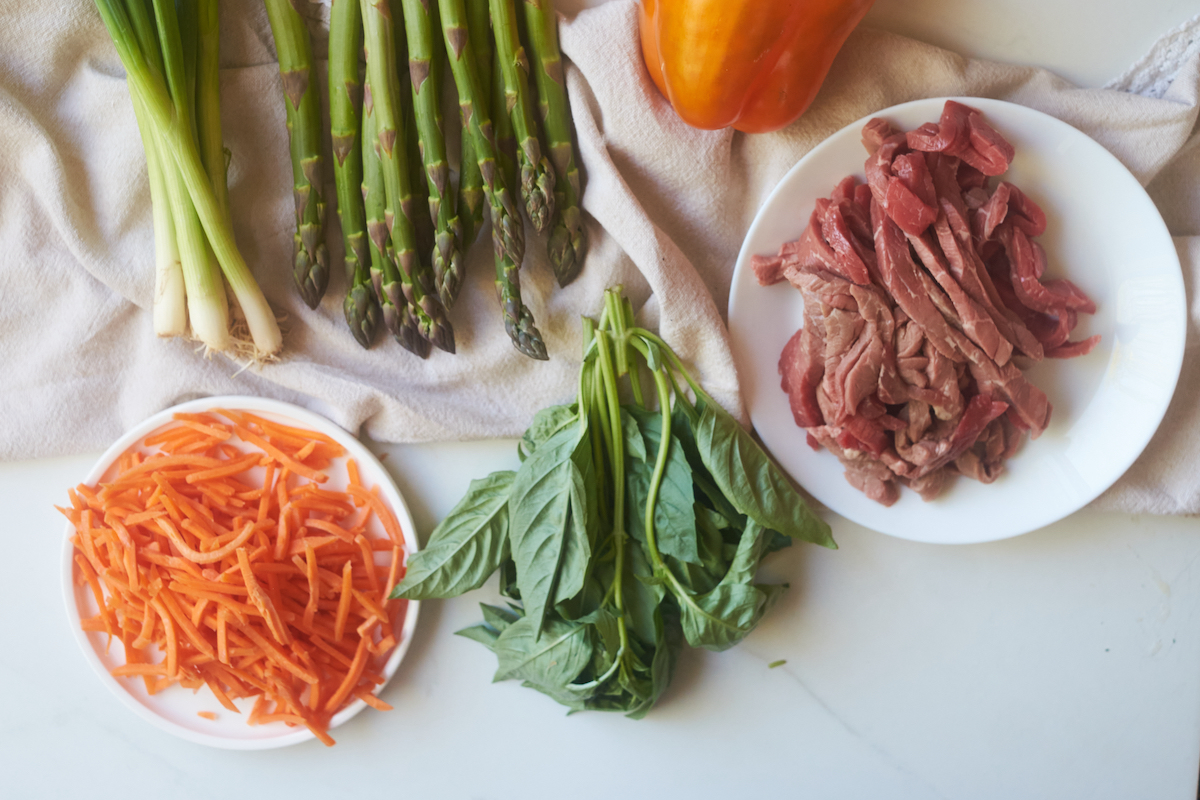 birdseye view of stirfry ingredients including basil, carrots, beef, pepper, green onions and asparagus