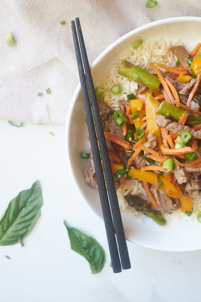 honey ginger beef and basil stirfry served over rice with chopsticks resting on the bowl