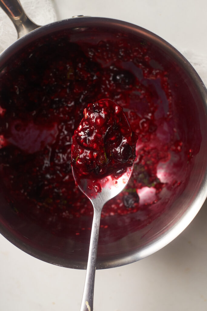 Spoon filled with basil berry compote over top of a pot filled with the compote being made