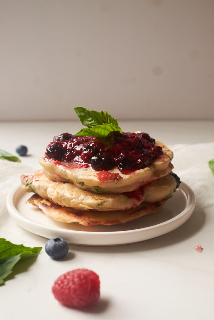 Side view of a stack of lemon basil pancakes topped with butter and basil berry compote