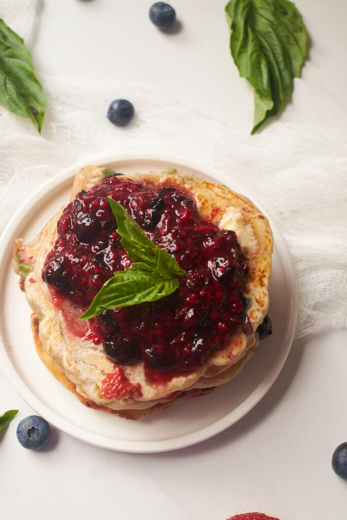 Birds eye view of a stack of lemon basil pancakes topped with butter and basil berry compote