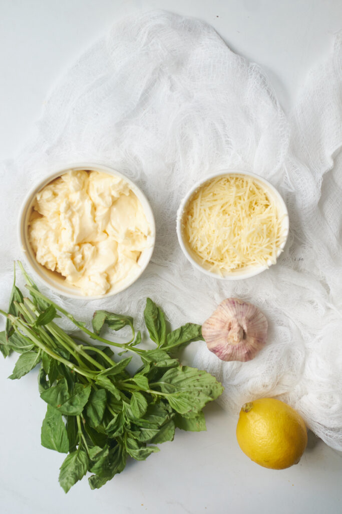 ingredients for basil aioli on a countertop including mayonnaise, garlic, parmesan, lemon and fresh basil
