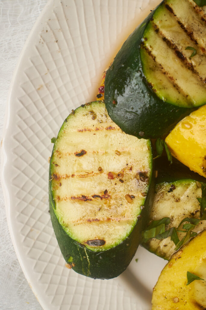 close up of grilled zucchini and summer squash with thai basil in a serving dish
