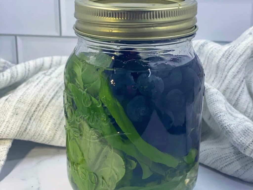 close up of vodka, blueberries and basil infusing in a mason jar
