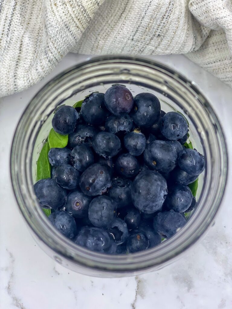 Birds eye view of basil leaves and blueberries in a jar before adding vodka to make a basil and blueberry vodka infusion
