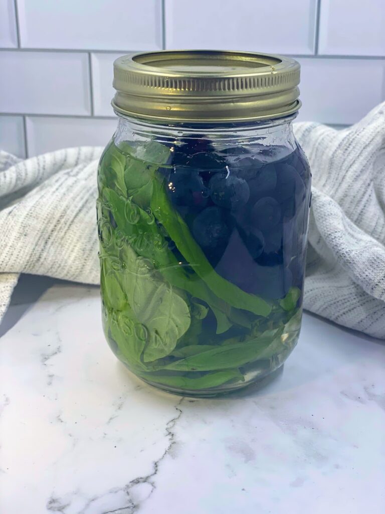 Vodka, basil leaves and blueberries in a tightly sealed mason jar, steeping to make basil blueberry vodka