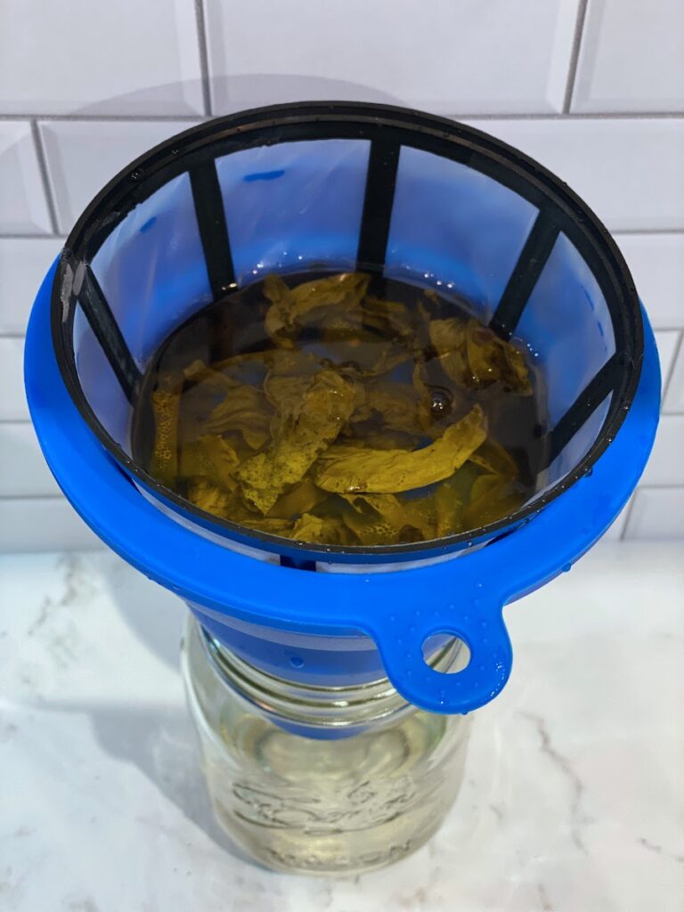 A reusable coffee filter catches basil leaves and blueberries that have steeped in a basil blueberry vodka infusion for several days