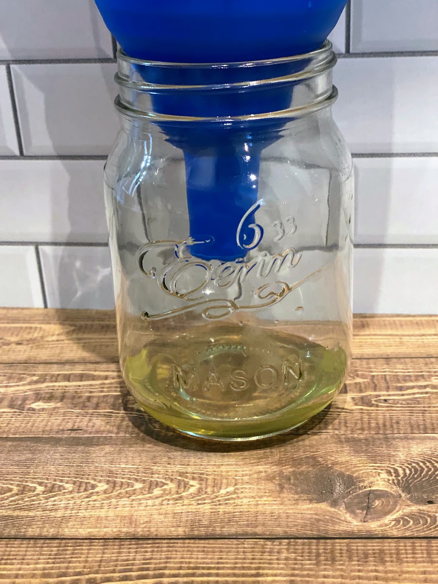 Lemon basil simple syrup strains through a funnel into a mason jar