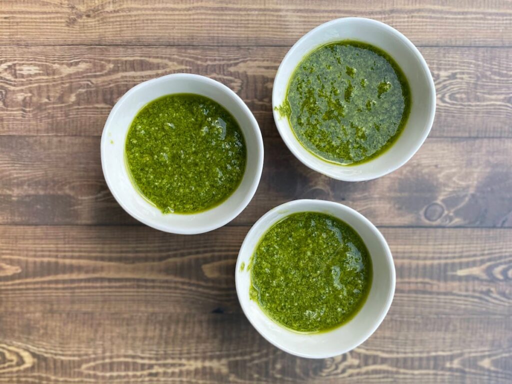 3 small bowls of homemade tuscany basil pesto on a wooden table